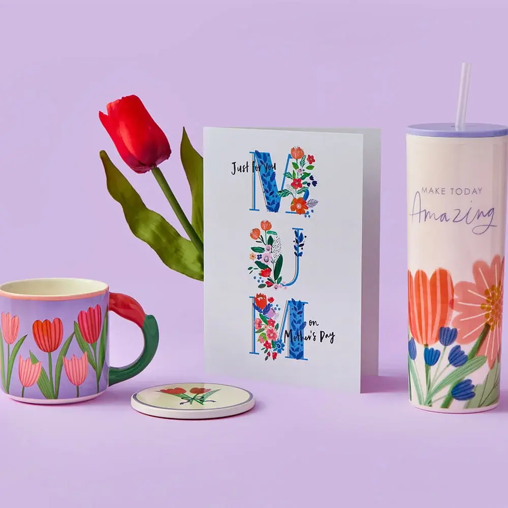 A floral Mother’s Day set featuring a pastel jug filled with pink and orange flowers, a butterfly‑decorated Grandma mug, and a garden‑themed Mum card arranged on a pastel purple background.